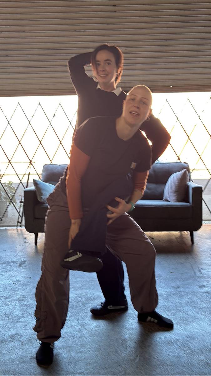 Two dancers in rehearsal, one giving the other a piggyback ride
